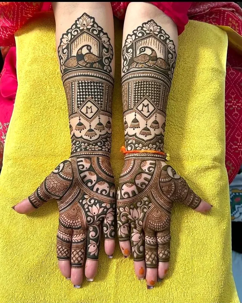 Bridal mehendi with peacock arch, jhumka and a letter M monogram on both arms