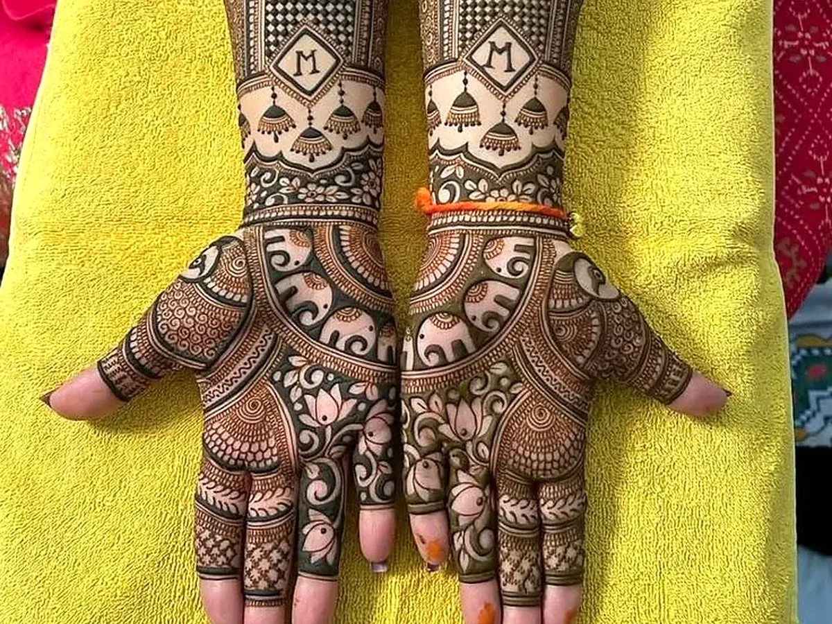 Bridal mehendi with peacock arch, jhumka and a letter M monogram on both arms